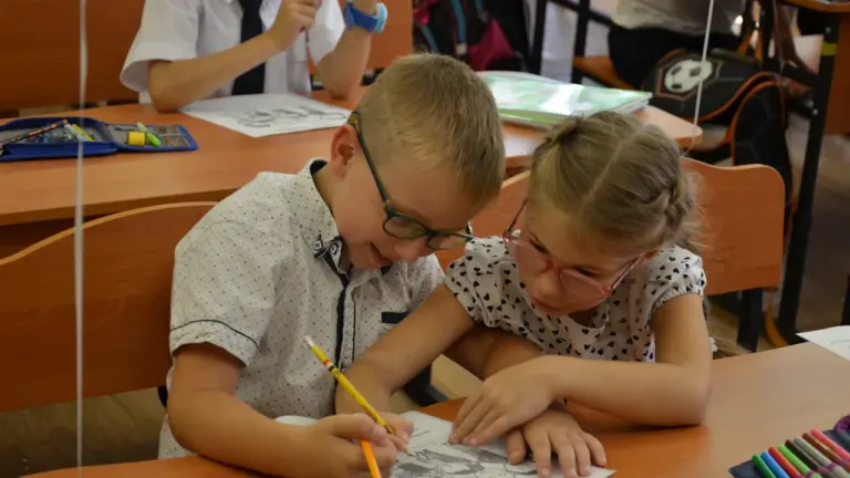 Dwoje uczniów szkoły podstawowej wspólnie rozwiązuje zadania w ławce podczas lekcji w klasie.