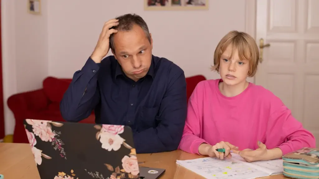 Zaniepokojony ojciec siedzący z córką przy laptopie podczas nauki w domu.