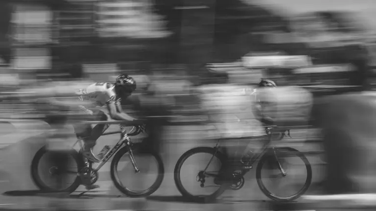 Dynamiczne ujęcie dwóch rowerzystów w ruchu, symbolizujące szybkie przemieszczanie się po mieście na rowerze.