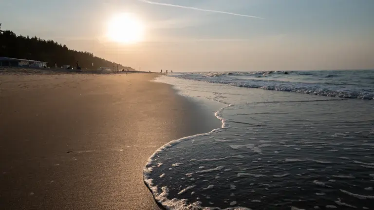 Słoneczna piaszczysta plaża o zachodzie słońca, symbolizująca letnie upały w Polsce.
