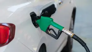 Pistolet dystrybutora paliwa wlewa benzynę do baku białego samochodu na stacji