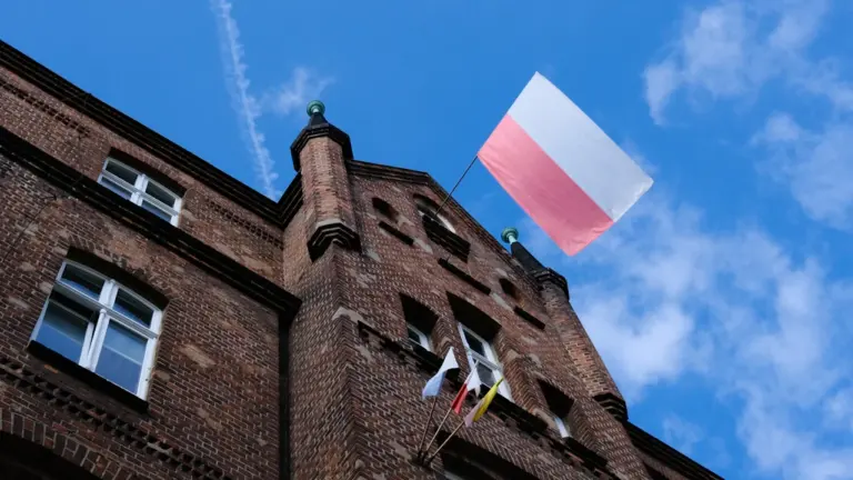 Polska flaga powiewająca na zabytkowym ceglanym budynku w Poznaniu pod błękitnym niebem.