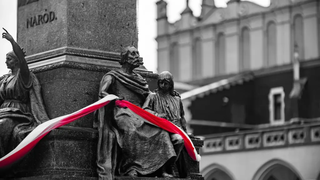 Pomnik w Krakowie ozdobiony biało-czerwoną flagą Polski w historycznym centrum miasta.