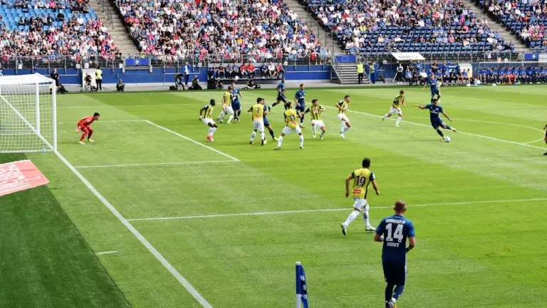 Piłkarze rozgrywający emocjonujący mecz piłki nożnej na dużym, zapełnionym stadionie sportowym.