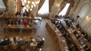 Wysoki kąt widzenia sali obrad z dużą grupą osób siedzących przy drewnianych stołach.
