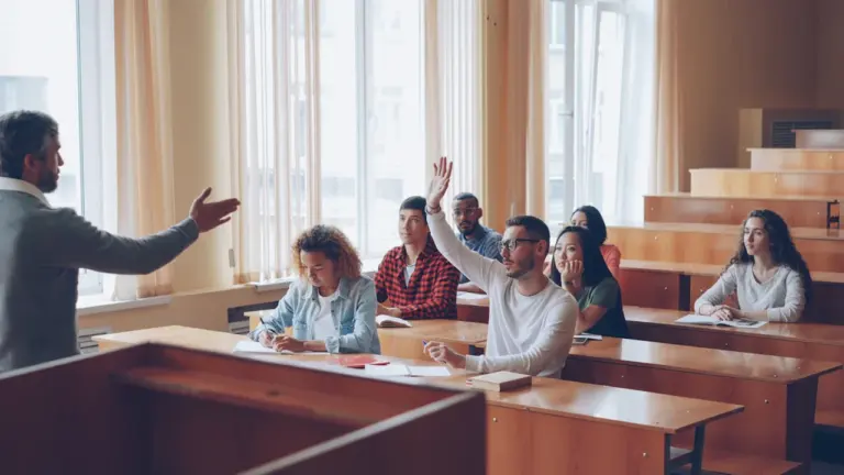 Student podnosi rękę w sali wykładowej podczas zajęć z nauczycielem w szkole wyższej.