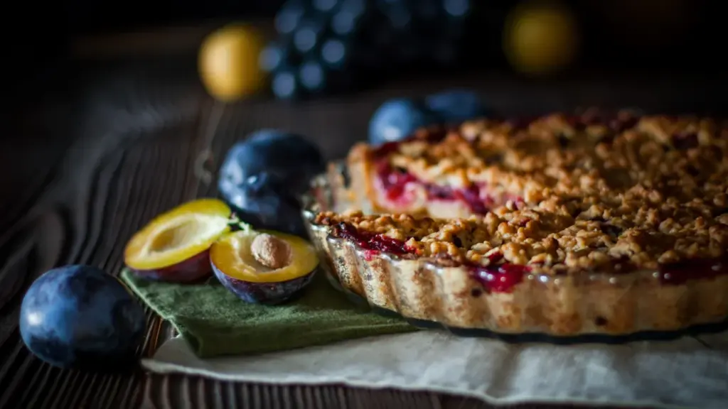 Apetyczna tarta ze śliwkami i kruszonką na drewnianym stole w stylu rustykalnym.