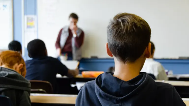 Uczeń w bluzie siedzący w szkolnej ławce podczas lekcji w klasie